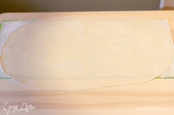 Постелите на стол полотенце и посыпьте его мукой. Немного раскатайте на нем тесто. Тесто очень пластичное, поэтому его нужно растягивать руками. Удобнее всего это делать на весу, затем постелить на полотенце и еще немного растянуть края. Если через тесто немного просвечивает полотенце, значит, достигнута идеальная толщина.