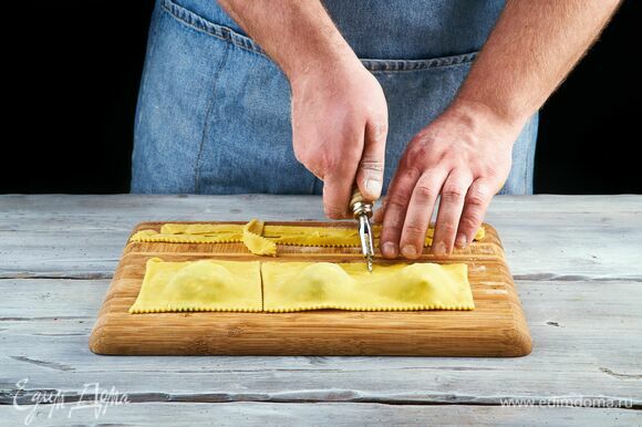 Скрепите края, а затем ножом разрежьте тесто на квадратики с начинкой посередине. Выложите равиоли в кипящую подсоленную воду и отварите до готовности.