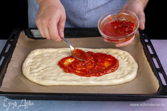 Смажьте тесто томатной пастой.
