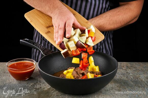 Через 50 минут тушения говядины добавьте к ней нарезанные овощи и протертые томаты. Тушите под крышкой 15 минут.