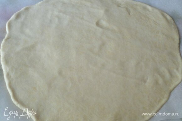 Достать тесто из холодильника. На подпыленном мукой столе раскатать тесто в круг толщиной примерно 5–6 мм. Перенести тесто на пергамент с помощью скалки.
