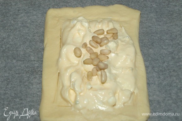 Мягкий соленый сыр смешать с яичным желтком. Если сыр не соленый, то добавьте соль по вкусу. Выкладываем сыр на тесто в обозначенных границах, сверху посыпаем кедровыми орехами.