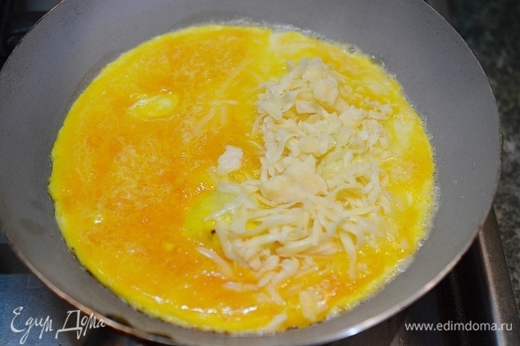 Когда омлет схватится по краям, половину омлета посыпьте сыром.