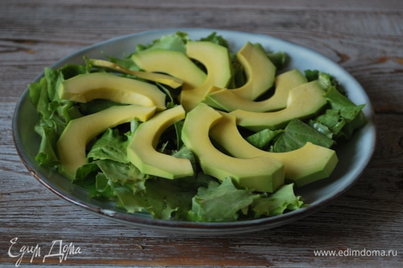 Салатные листья вымойте, крупно нарежьте и выложите на тарелку. Авокадо почистите, удалите косточку, нарежьте дольками и выложите сверху на салатные листья.