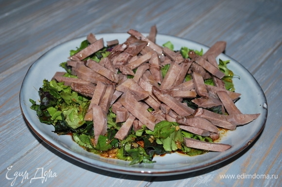 Полейте заправкой салатные листья, добавьте нарезанный язык, посыпьте свежемолотым черным перцем, перемешайте.