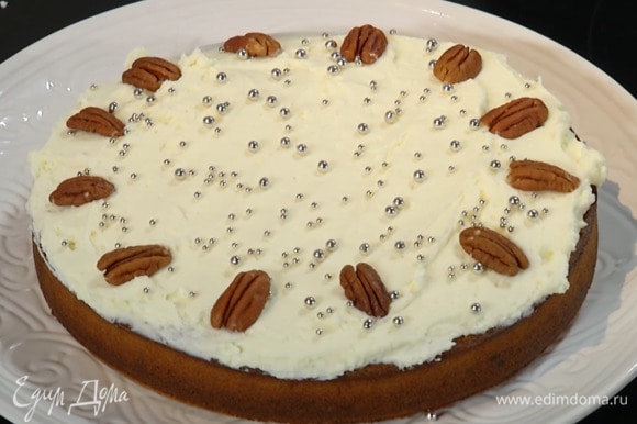 Остывший пирог смазать кремом, посыпать кондитерскими украшениями и выложить по кругу орехи пекан.