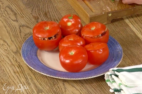 Плотно нафаршировать помидоры начинкой, накрыть крышечками и поместить в глубокую сковороду или форму для запекания.