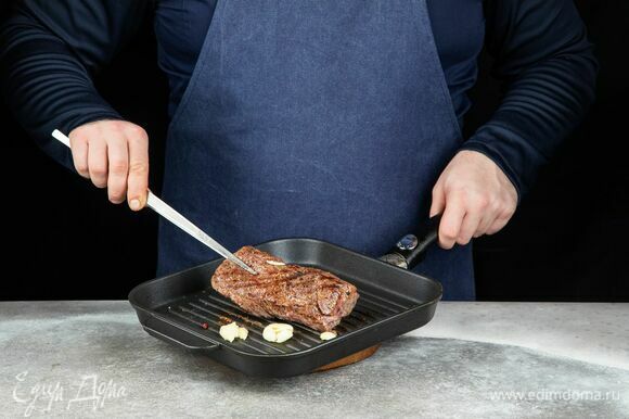 Обжарьте мясо с чесноком на сковороде-гриль от 5 до 8 минут с каждой стороны до желаемой прожарки. Во время обжаривания стейк периодически переворачивайте. Готовое мясо подсушите полотенцем, чтобы убрать лишний сок. Нарежьте тонкими слайсами.