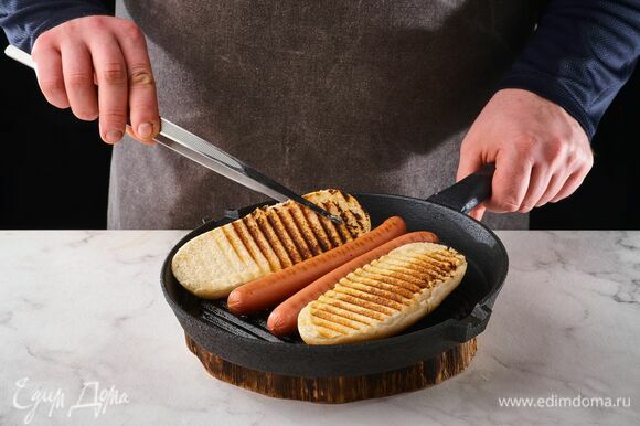 Булочки для хот-догов разрежьте в середине и поджарьте вместе с сосисками на сковороде-гриль с двух сторон по 1 минуте.