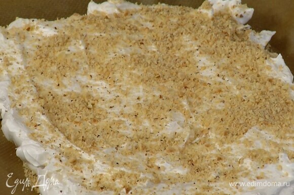 Застеленный бумагой для выпечки противень посыпать частью ореховой крошки, выложить белковую массу, разровнять и присыпать оставшимися измельченными орехами.