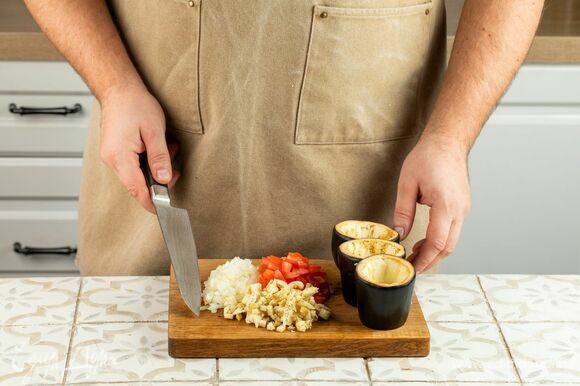 Нарежьте мелко лук и помидоры. У баклажанов срежьте верхушки. Каждый разделите на 3 части и аккуратно выньте сердцевину с помощью ножа или ложки-нуазетки. Мякоть нарежьте кубиками.