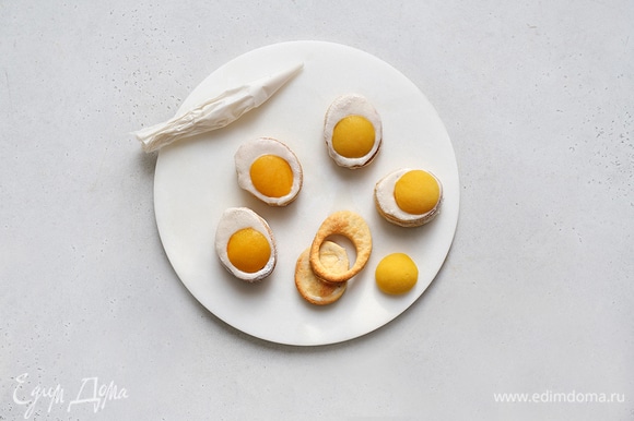 Смажьте все печенья глазурью и соберите: на целые заготовки выложите печенья с дырочкой, в центр поместите по половинке персика.