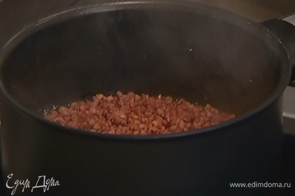 Гречку всыпать в тяжелый сотейник и залить горячей водой, так чтобы крупа была покрыта жидкостью. Накрыть крышкой и готовить 7–8 минут, пока вода не выкипит, затем выключить огонь и оставить гречку доходить под крышкой.